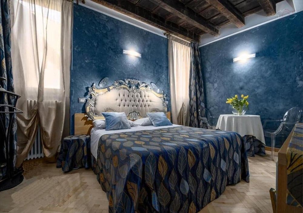 A cozy hotel room with blue textured walls, an ornate bed, wooden beams, and soft lighting creates a luxurious and inviting atmosphere perfect for travelers seeking comfort and style.