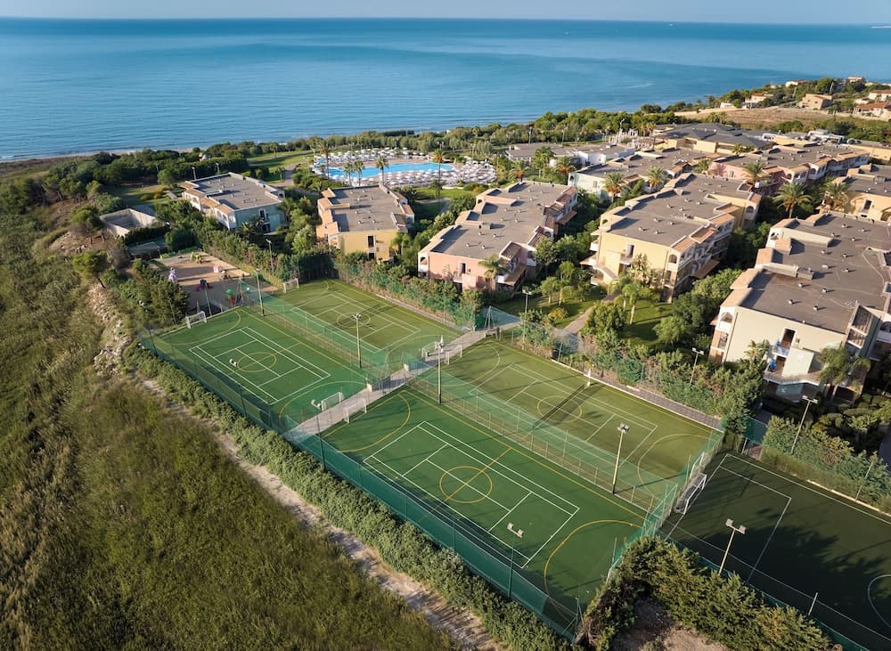An aerial view of vibrant green sports fields nestled among residential buildings near the serene ocean, ideal for travelers seeking an active coastal getaway.