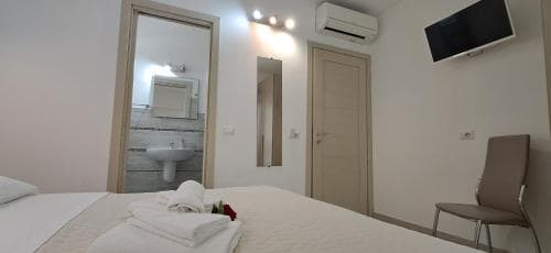 A cozy hotel room features a neatly made bed, a modern bathroom visible through an open door, a mounted TV, and a comfortable chair, ideal for travelers seeking a clean and functional accommodation.