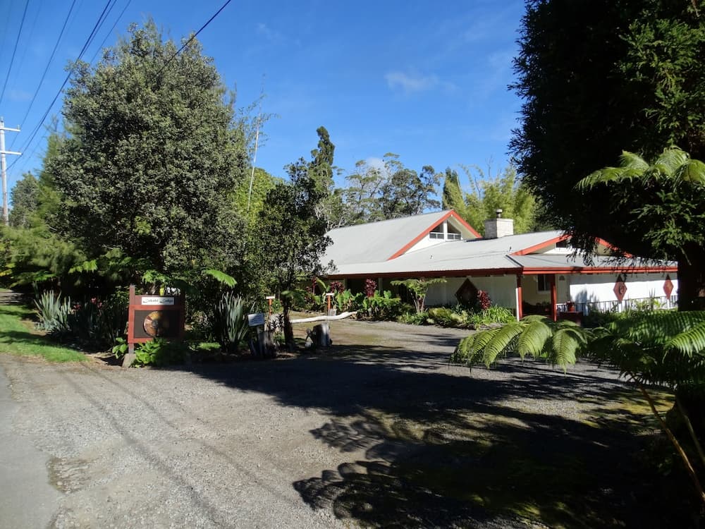A serene rural retreat features a charming white house with red trim surrounded by lush greenery, ideal for travelers seeking a peaceful getaway in nature.