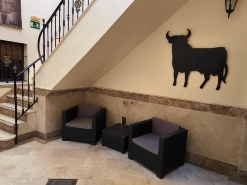 A cozy hotel lobby features modern black armchairs under a staircase adorned with a bull silhouette, creating an inviting atmosphere for travelers seeking relaxation.