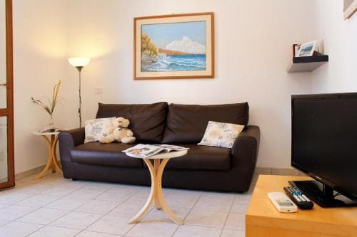 A cozy living room with a brown sofa adorned by pillows and a teddy bear, framed ocean artwork on the wall, and modern furnishings creates a welcoming atmosphere ideal for travelers seeking comfort in a vacation rental.