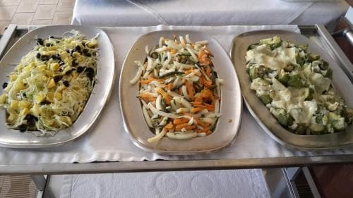 A vibrant buffet spread featuring colorful salads on metal trays atop a white tablecloth sets a cheerful dining mood, ideal for travelers seeking healthy meal options at a resort or cruise ship.