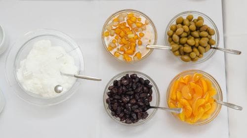 A serene breakfast spread featuring yogurt, corn kernels, olives, raisins, and apricots in glass bowls on a white tablecloth, ideal for a healthy morning meal during a wellness retreat.