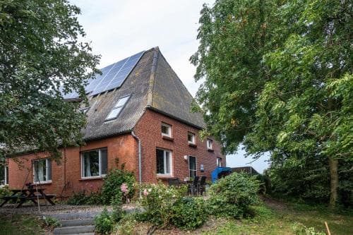 A cozy brick house nestled among lush greenery with solar panels on its roof offers a serene retreat, ideal for eco-conscious travelers seeking a peaceful countryside getaway.