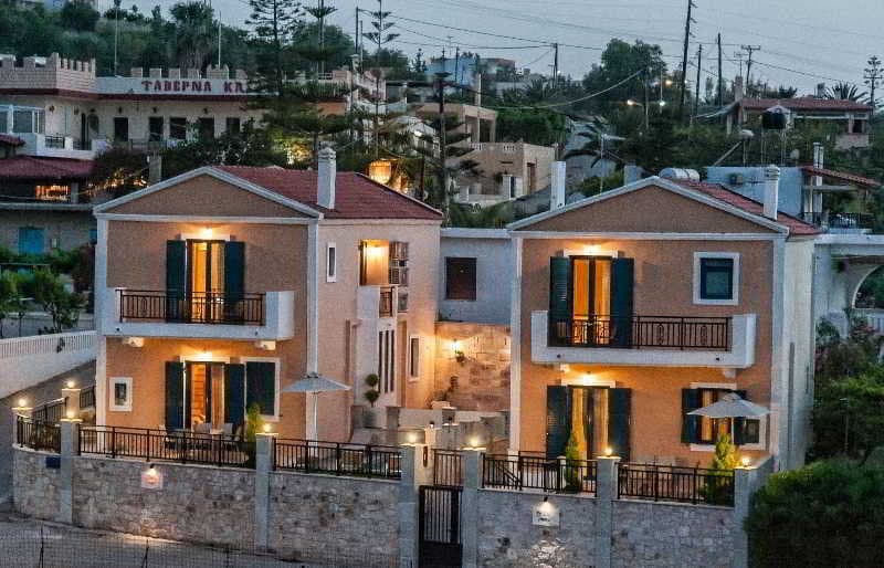 Charming Mediterranean-style villas with warm lighting and balconies overlook a tranquil coastal village at dusk, ideal for travelers seeking a cozy retreat in a picturesque setting.