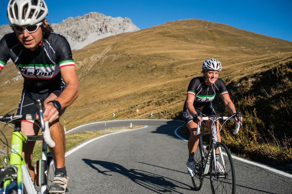 Two cyclists pedal along a winding mountain road under a clear blue sky, showcasing an adventurous outdoor activity ideal for fitness enthusiasts exploring scenic landscapes.