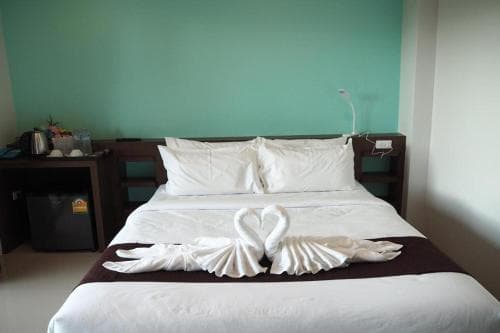 A cozy hotel room features a neatly made bed adorned with swan-shaped towels, set against a calming teal wall, ideal for travelers seeking comfort and relaxation.