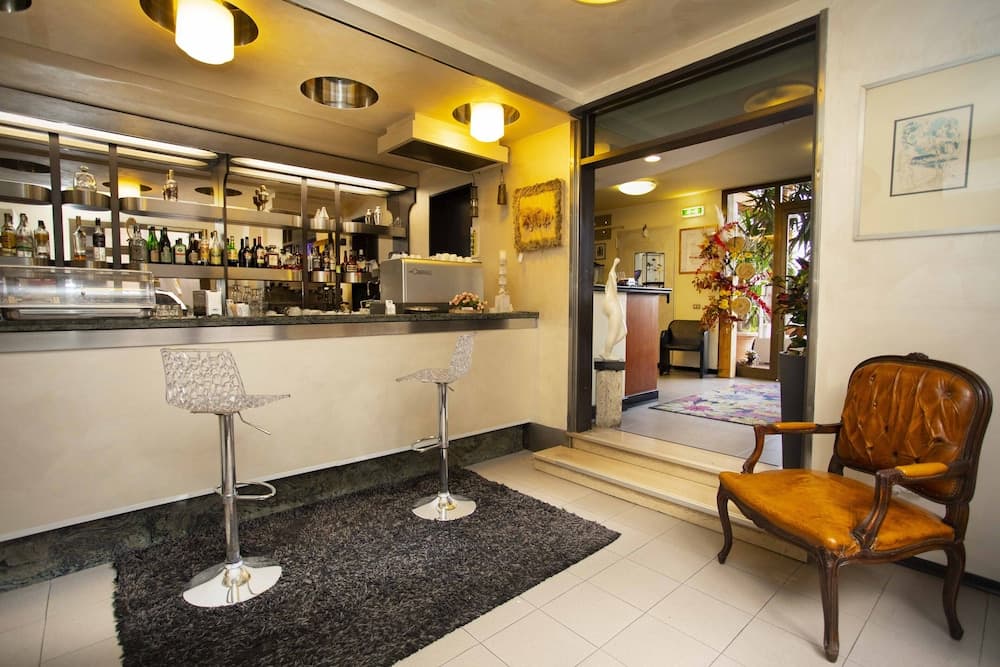 A cozy bar area with modern stools on a plush rug, warm lighting, and a vintage leather chair invites travelers to unwind in a stylish urban retreat.