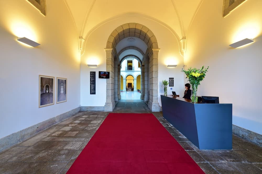 A warmly lit historical corridor with arched doorways, a vibrant red carpet, and a reception desk creates an inviting atmosphere ideal for cultural tourism and event hosting.