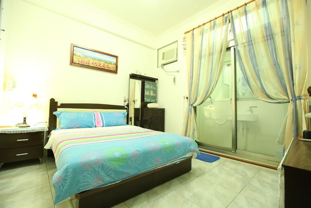 A cozy hotel room features a neatly made bed with vibrant floral bedding, soft lighting, and a glass-enclosed bathroom, ideal for travelers seeking comfort and convenience.