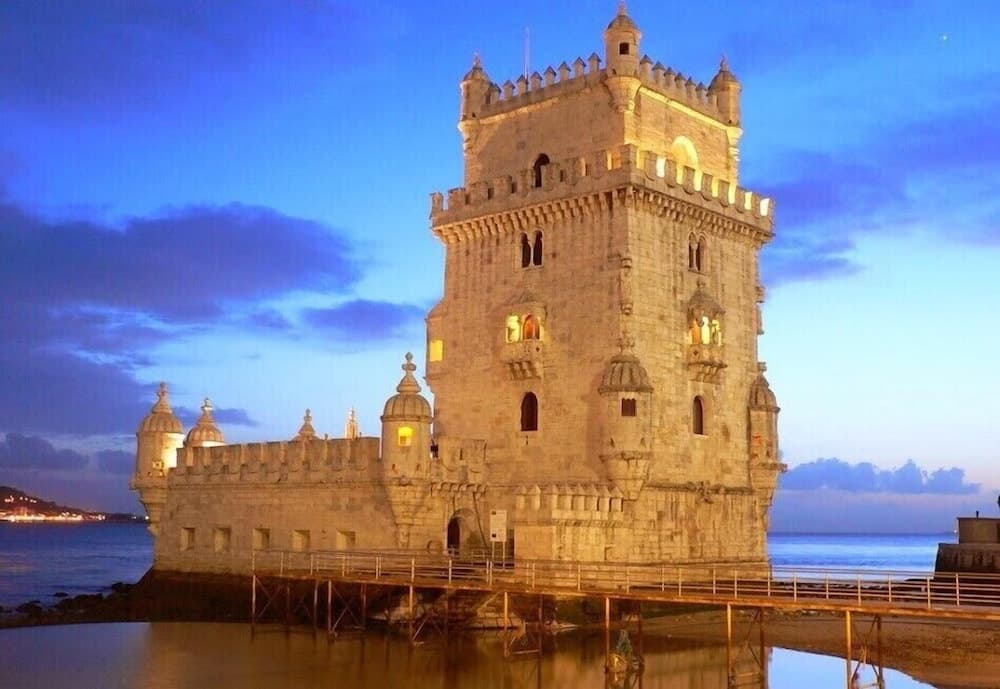 A majestic medieval tower illuminated against a twilight sky stands by the water's edge, offering travelers a serene and historic backdrop for photography and exploration.