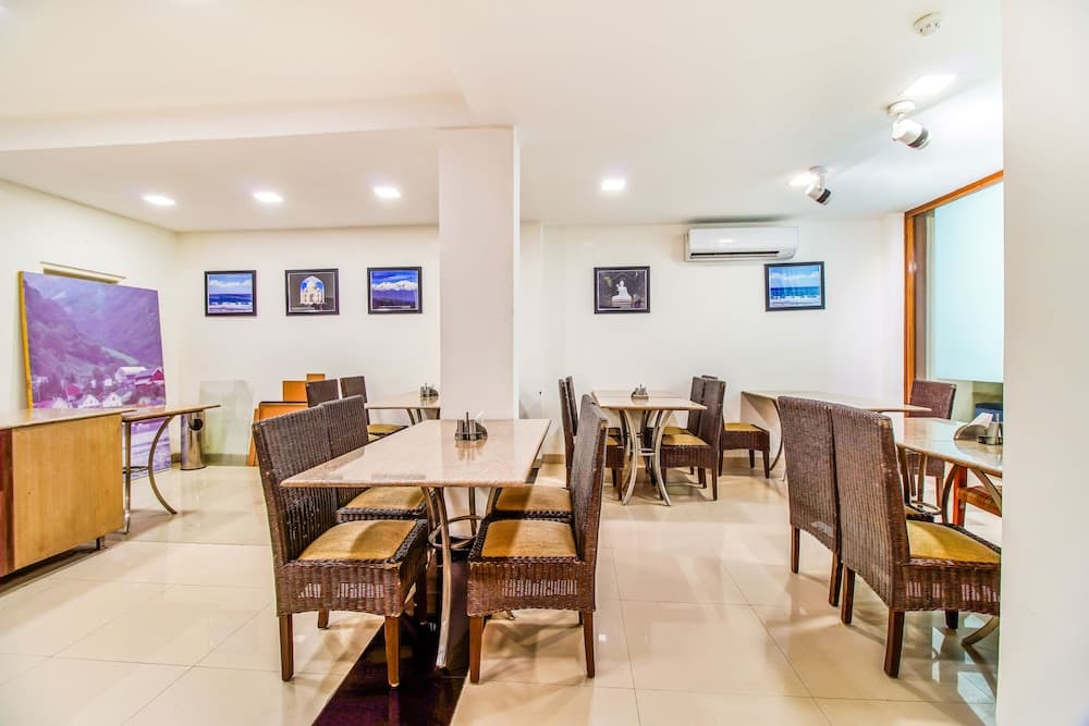 A cozy indoor dining area with wicker chairs, framed artwork on white walls, and a serene ambiance is ideal for travelers seeking a comfortable spot to enjoy meals or relax during their stay.