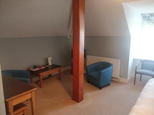 A cozy attic room with slanted ceilings, blue armchairs, wooden furniture, and soft lighting creates a serene atmosphere ideal for a quiet retreat or work-from-home setup.