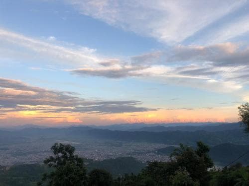 A serene sunset view from a hilltop overlooking a sprawling valley city framed by distant mountains, ideal for tranquil nature escapes and scenic photography.