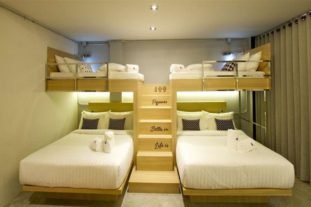 A cozy hostel room features bunk beds and double beds with modern lighting and motivational wall art, ideal for budget travelers seeking comfort and camaraderie.