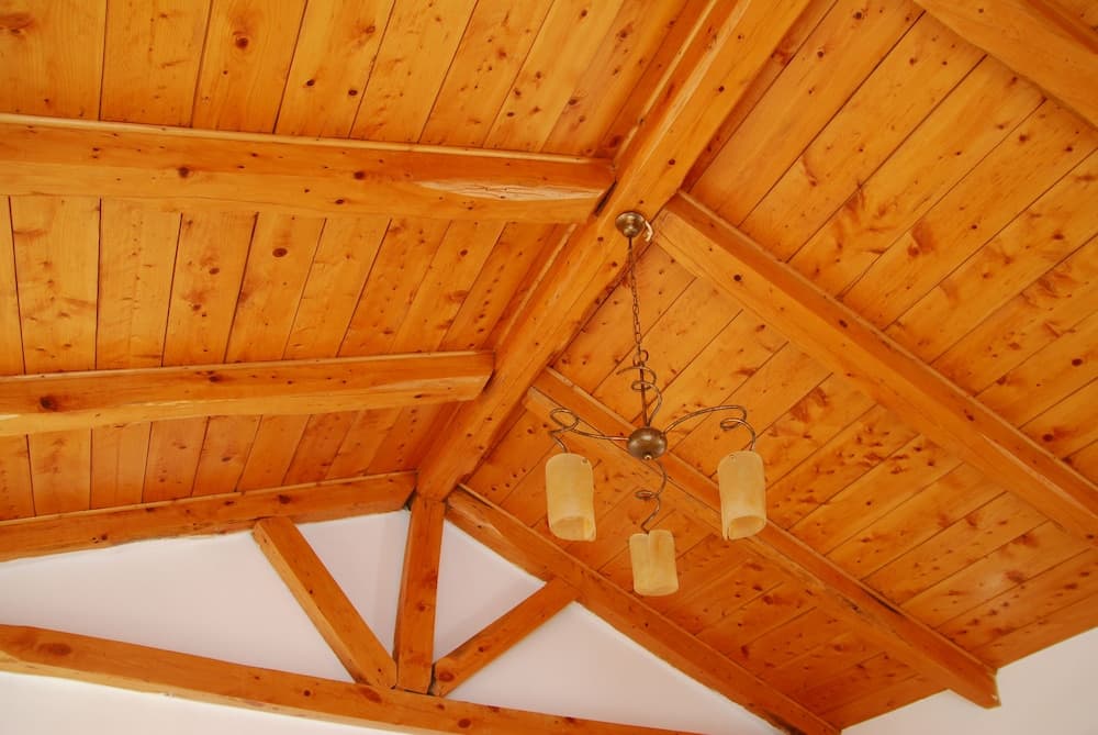 A cozy indoor space features a rustic wooden ceiling with exposed beams and a charming chandelier, ideal for travelers seeking a warm and inviting atmosphere in a cabin or lodge setting.