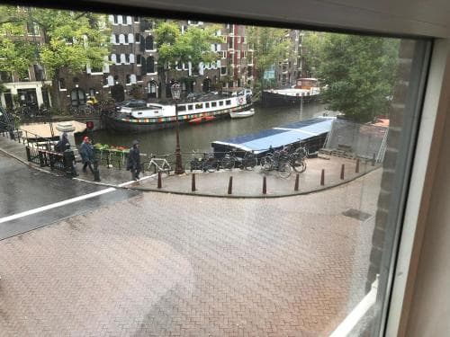 A serene canal-side view from a tram window captures cobblestone streets, parked bicycles, and traditional Dutch architecture, evoking a tranquil urban exploration in Amsterdam.