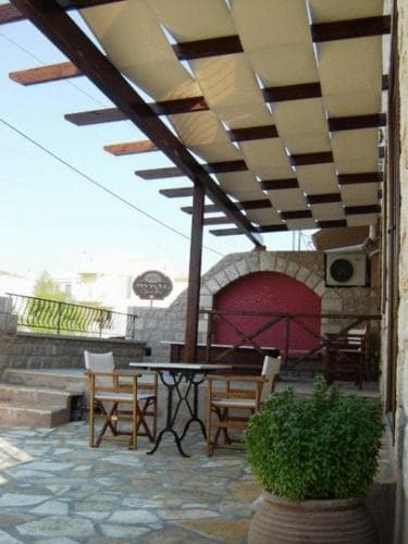 A cozy outdoor terrace with stone flooring, wooden pergola, and potted greenery offers a serene spot for travelers to relax and enjoy meals in a Mediterranean setting.