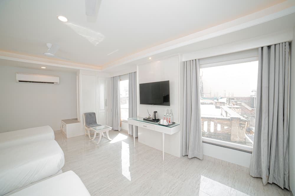 A serene hotel room with white marble floors, minimalist furniture, and large windows offering a view of rooftops, ideal for travelers seeking comfort and simplicity.