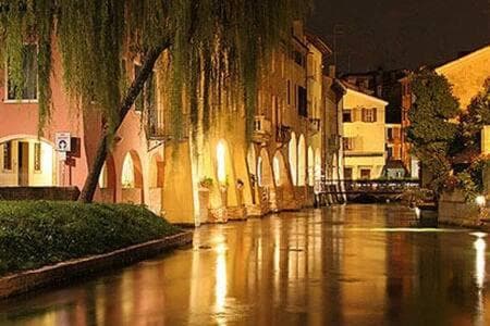 A serene nighttime canal scene illuminated by warm lights, featuring charming European-style buildings, weeping willows, and reflective water, ideal for romantic getaways or cultural exploration.