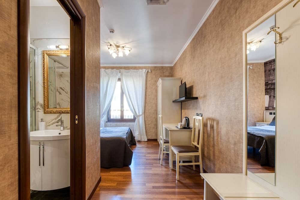 A cozy hotel room with warm wooden floors, a neatly made bed by the window, a desk with a TV, and an adjacent bathroom featuring a modern sink and mirror, ideal for travelers seeking comfort and convenience.