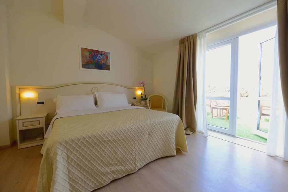 A cozy hotel bedroom with a neatly made bed, warm lighting, and a sliding glass door leading to a sunny outdoor patio, ideal for travelers seeking comfort and relaxation.
