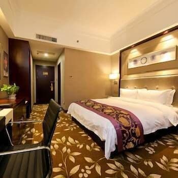 A cozy hotel room features a neatly made bed with patterned bedding, a desk with a chair, and warm lighting, creating an inviting atmosphere ideal for travelers seeking comfort and relaxation.