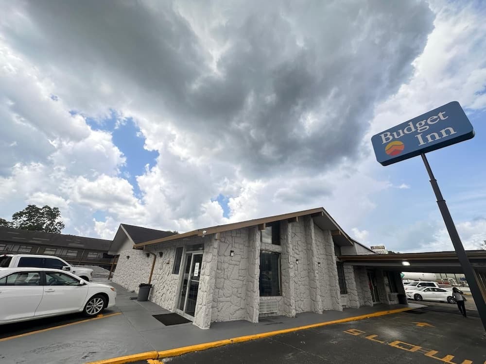 A Budget Inn with a stone facade stands under a dramatic cloudy sky, offering travelers a budget-friendly accommodation option in a roadside setting.