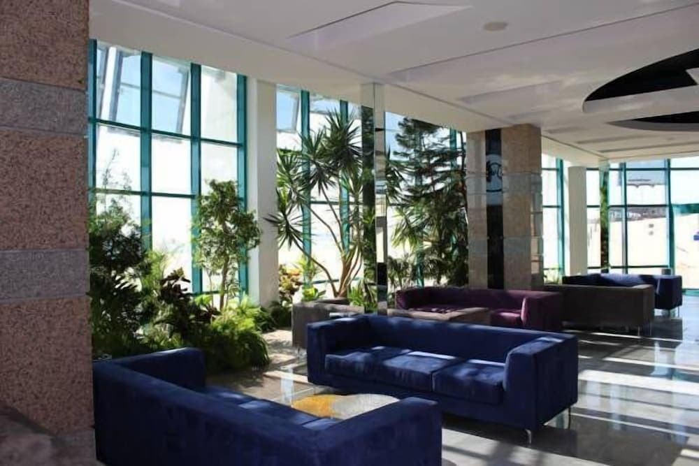 A modern hotel lobby features plush blue sofas, lush greenery, and large windows that flood the space with natural light, creating an inviting atmosphere ideal for travelers seeking relaxation and comfort.