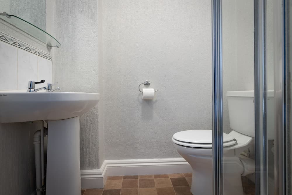 A clean and minimalistic bathroom features a white pedestal sink, toilet, and glass shower enclosure, ideal for travelers seeking a simple and functional accommodation space.