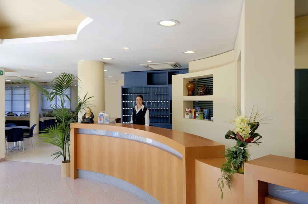 A welcoming hotel lobby features a curved reception desk adorned with fresh flowers and plants, set against a modern interior with warm lighting, ideal for travelers seeking a comfortable check-in experience.