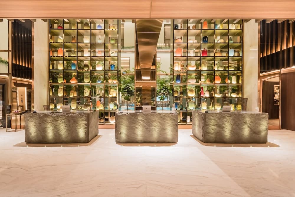 A luxurious hotel lobby features sleek stone reception desks illuminated by ambient lighting, surrounded by vibrant shelves of colorful vases, creating an elegant and inviting atmosphere ideal for travelers seeking upscale accommodations.