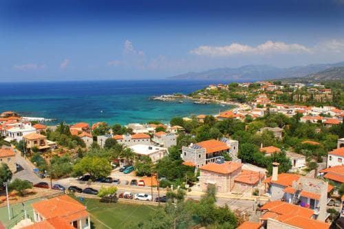 A picturesque coastal village with vibrant orange-roofed houses nestled among lush greenery overlooks the serene turquoise sea, ideal for travelers seeking a tranquil seaside retreat.