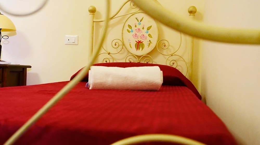 A cozy bedroom with a red bedspread, ornate yellow metal headboard featuring floral designs, and a warm ambiance is ideal for travelers seeking a charming and comfortable accommodation.