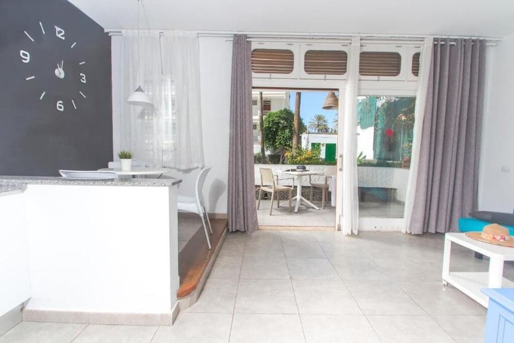 A cozy apartment interior with a modern kitchen, large clock wall art, and an inviting patio view through open doors, perfect for travelers seeking a comfortable and stylish vacation rental.