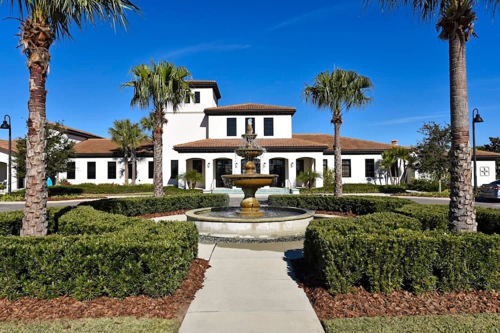 A serene Mediterranean-style building framed by palm trees and lush greenery, featuring a central fountain under a clear blue sky, ideal for a relaxing vacation retreat.