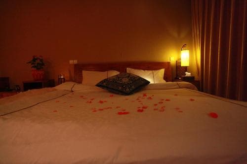 A cozy hotel room with a warmly lit ambiance features a bed adorned with rose petals, ideal for romantic getaways.