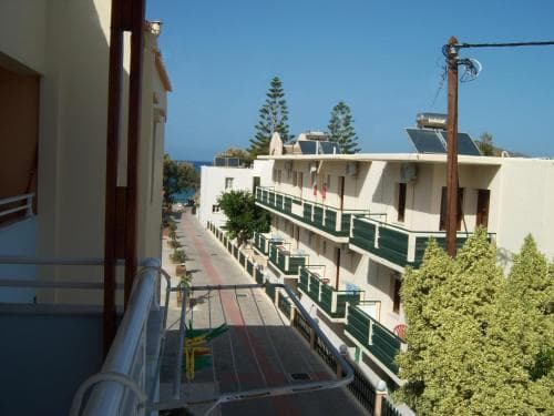 A serene coastal resort scene features balconied buildings lined along a narrow street, framed by lush greenery under a clear blue sky, ideal for travelers seeking a tranquil seaside getaway.