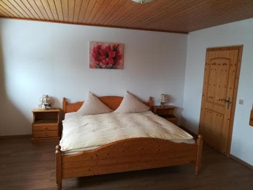 A cozy bedroom with wooden furnishings, a floral wall art, and warm lighting creates an inviting atmosphere ideal for travelers seeking a comfortable retreat.