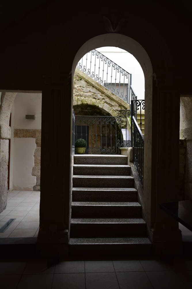 A serene stone staircase framed by an arched doorway leads to a sunlit courtyard, perfect for exploring historic architecture and capturing atmospheric photography.