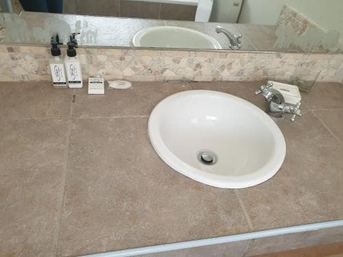 A clean hotel bathroom sink with tiled countertop, mirror, toiletries, and modern fixtures offers a practical space for travelers to refresh during their stay.