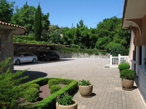 A serene courtyard with parked cars, lush greenery, and potted plants under a sunny sky offers a tranquil setting ideal for a relaxing vacation retreat.