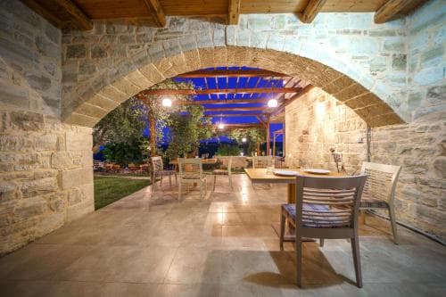 A cozy outdoor dining area framed by a rustic stone archway, featuring wooden chairs and tables under warm lighting, evokes a serene evening ambiance ideal for travelers seeking relaxation at a charming retreat.