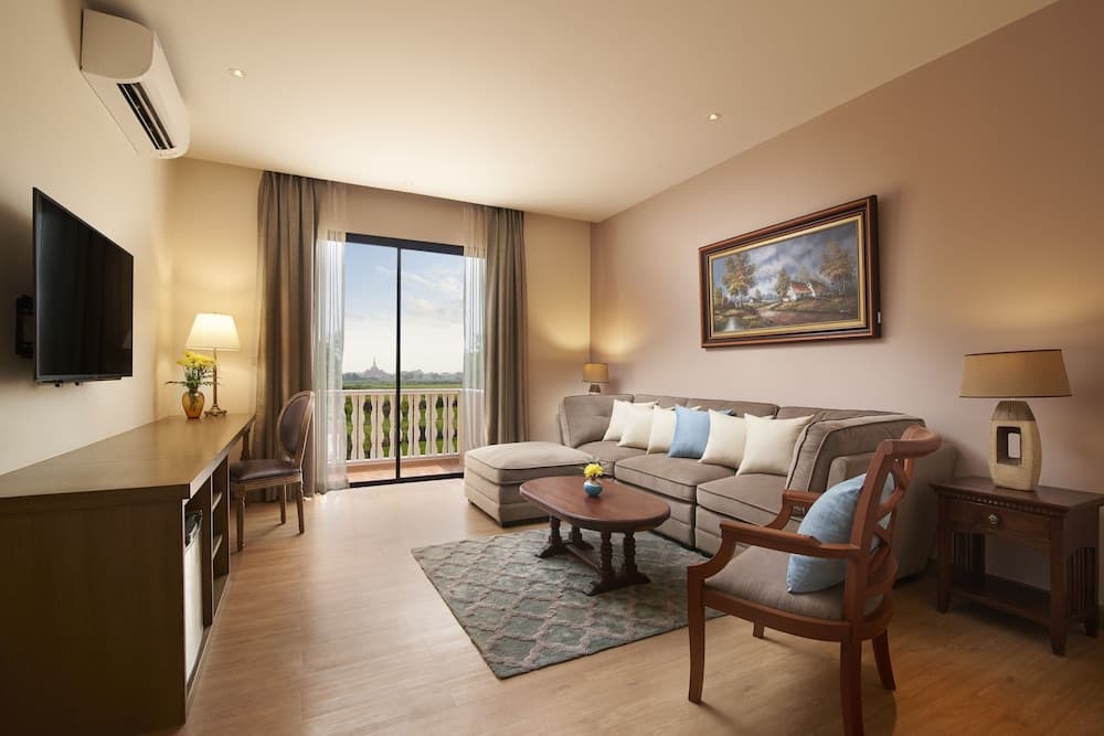 A cozy hotel suite features warm lighting, a plush sofa, wooden furnishings, and a balcony view, ideal for travelers seeking comfort and relaxation during their stay.