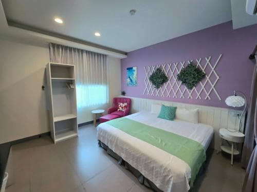 A cozy hotel room features a neatly made bed with green accents, a purple wall adorned with decorative plants, and soft lighting, creating a welcoming atmosphere ideal for travelers seeking comfort and relaxation.