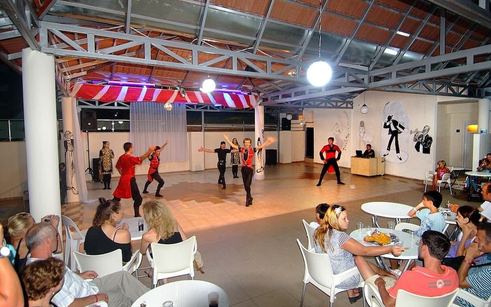 A lively indoor dance performance captivates an audience in a spacious venue adorned with vibrant decorations, ideal for cultural exploration and entertainment.