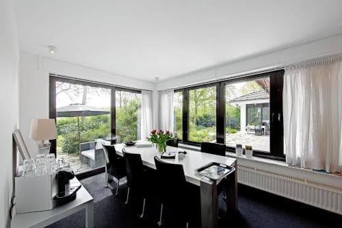 A modern dining area with sleek black furniture and large windows offering a serene view of lush greenery, ideal for travelers seeking a tranquil retreat in a contemporary lodge setting.