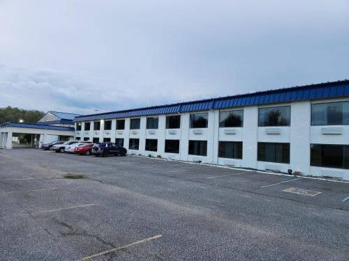 A quiet roadside motel with white brick walls and blue trim under an overcast sky offers travelers a simple stay with ample parking and a calm atmosphere.
