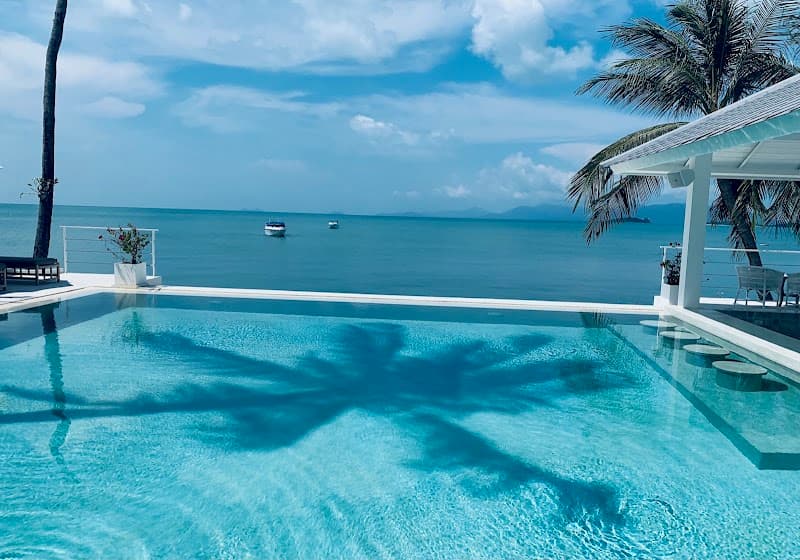A serene tropical beach resort features an infinity pool reflecting palm trees under a clear blue sky, ideal for luxury relaxation and vacation photography.